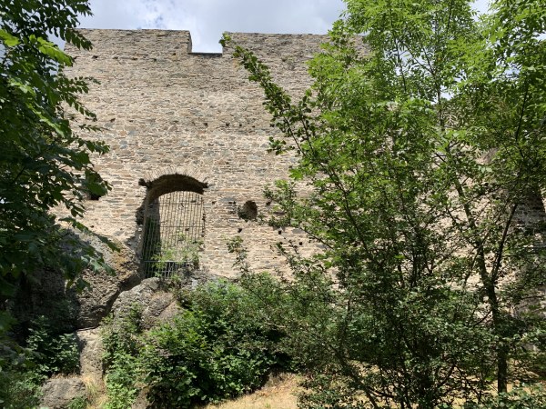 Burgruinenmauer mit vergittertem Durchgang hinter Bumen