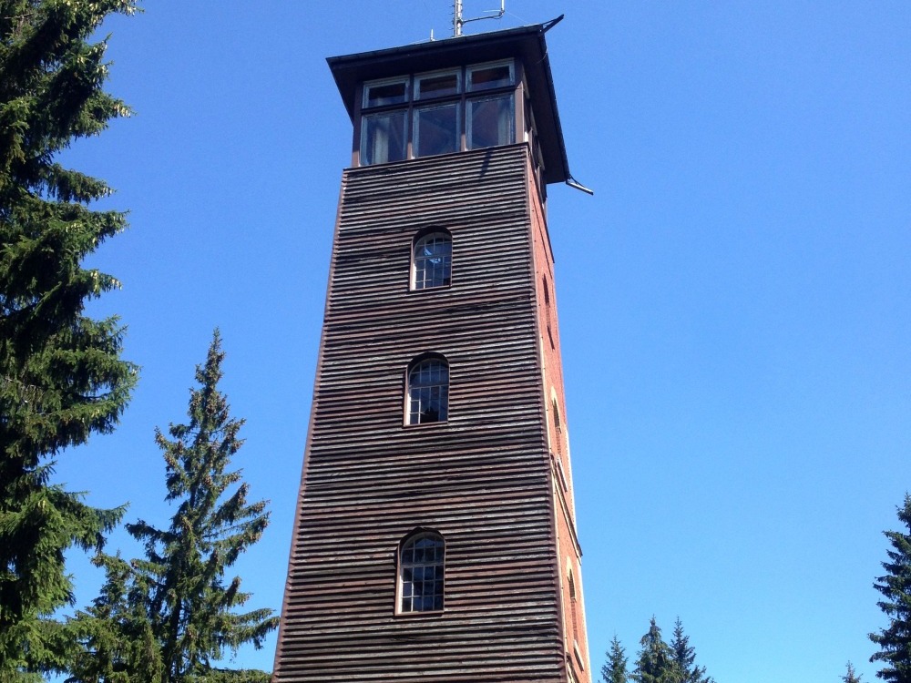 Turm hinter Teil einer Htte. Auf dem Turm befindet sich eine Sende-Antenne. Links und rechts stehen Bume.