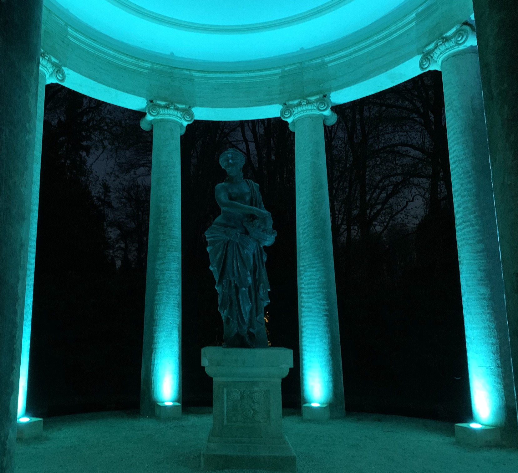 Statue trkisblau angeleuchtet vor Sulen. Dahinter die Nacht.