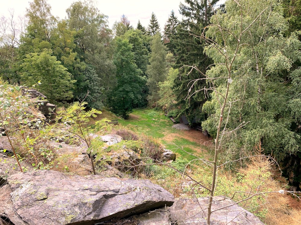 Blick von einem Felsen nach unten. Mitten im Wald. Unten steht eine Htte und Bnke.