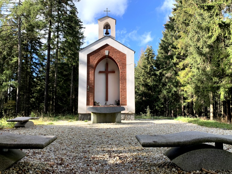Kleine Kapelle im Wald vor Kieselsteinen und Steinbänken