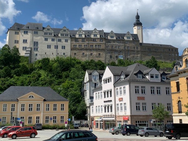 Parkplatz mit architektonisch wertvollen Häusern. Auf dem Berg das Obere Schloss von Greiz: Mehrere zusammengesetzte Häuser auf einer Anhöhe