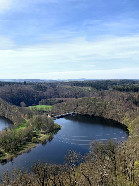 Talsperre in waldiger Landschaft. Rechts großes Schloss.