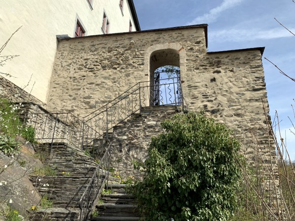 Fußgängertorbogen durch Steinmauer. Mit Geländer geführte Steintreppe nach unten.