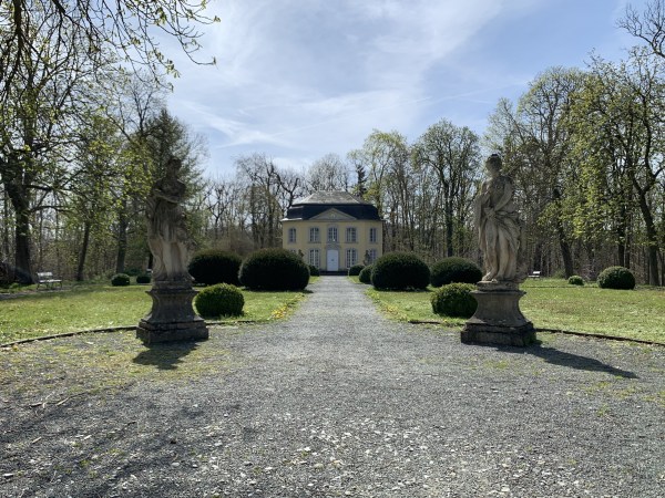 Weg zum Gartenhaus durch Statuen und Büsche. Der Rasen an den Seiten ist gepflegt. Das Gras ist gemäht, die Bäumne sind schön geschnitten.