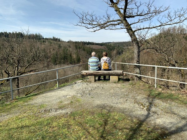 Aussichtspunkt mit Bank und Geländer. Auf der Bank sitzt ein älteres Ehepaar, was den Ausblick genießt. 