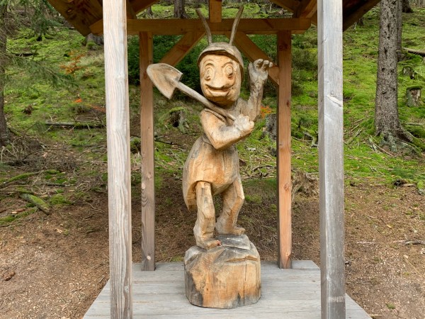 Große überdachte Holzfigur einer stehenden Ameise mit Schaufel.