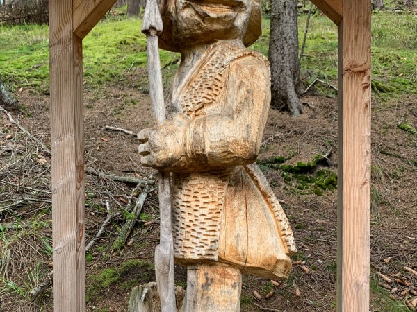 Große überdachte Holzfigur einer stehenden Ameise mit Speer.